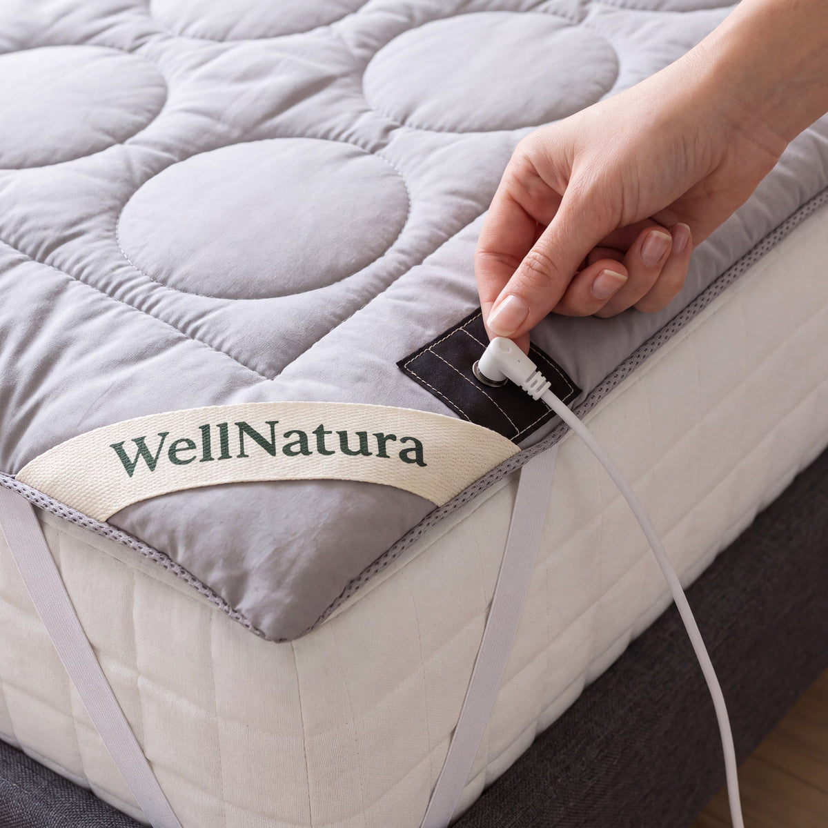 Hand clipping the white grounding cable onto the snap of the WellNatura topper