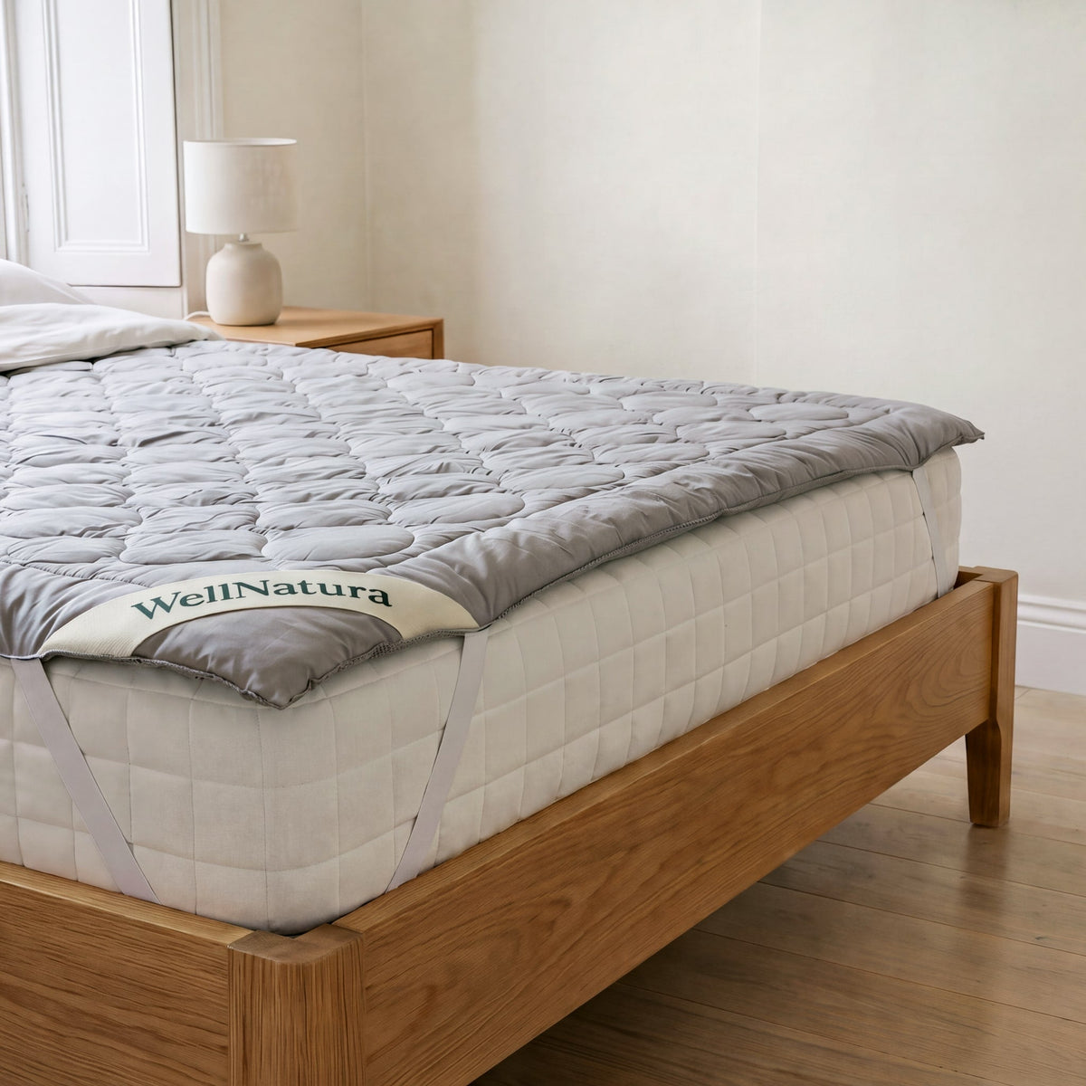 WellNatura grounding topper fitted on a white mattress, foot corner with the WellNatura label